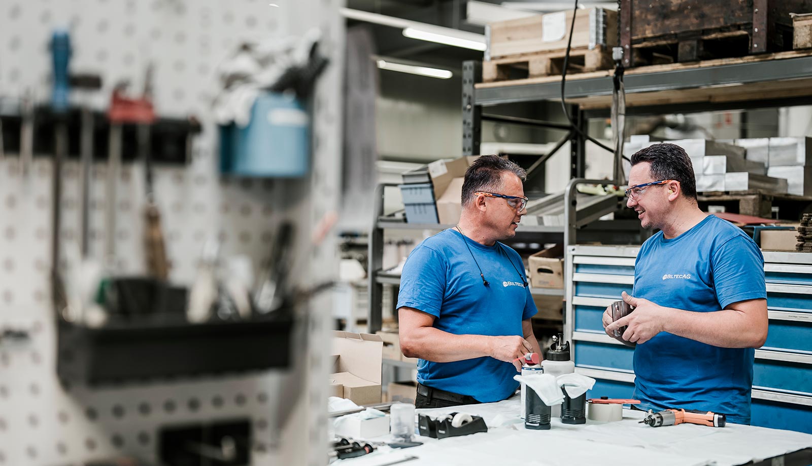 Employees of Biltec AG in a technical discussion, standing in the workshop, expressed through satisfied and happy body language. The scene illustrates the positive working atmosphere and cooperative teamwork in the company's production hall.